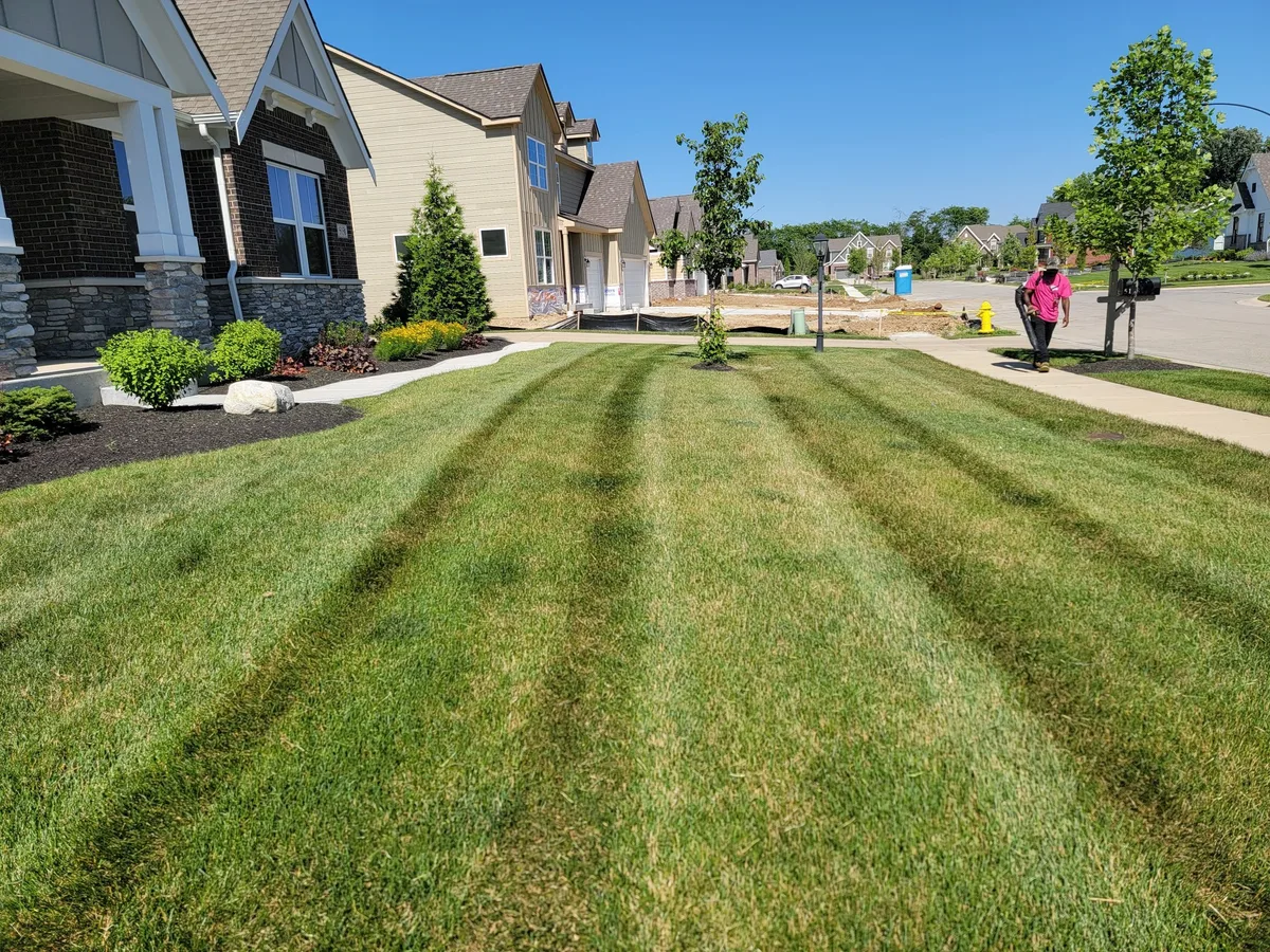 Sprout crew member in pink shirt mowing a commercial property